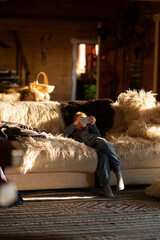 Blonde teen plays a game on the phone sitting on a cozy sofa in a country house