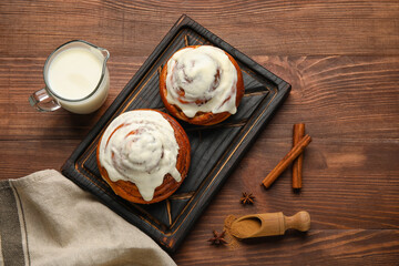 Board of tasty cinnamon rolls with cream on wooden background