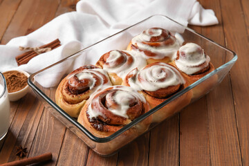 Baking dish of tasty cinnamon rolls with cream on wooden background
