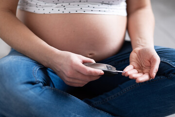 A pregnant woman measures her blood sugar level by puncturing her finger with a lancet while sitting on the floor