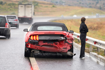 Accident on the road. A broken-down Ford Mustang convertible with a female car driver standing next...
