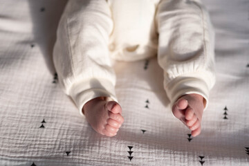 Charming legs of a newborn baby lying on a bright bed in the light of the bright sun