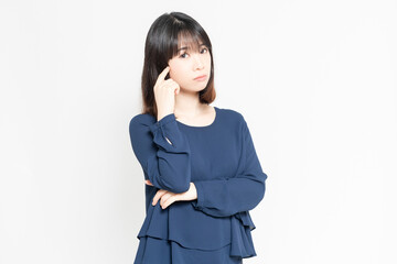 白い背景の前に立って、腕を組んで考え事をしている若い女性