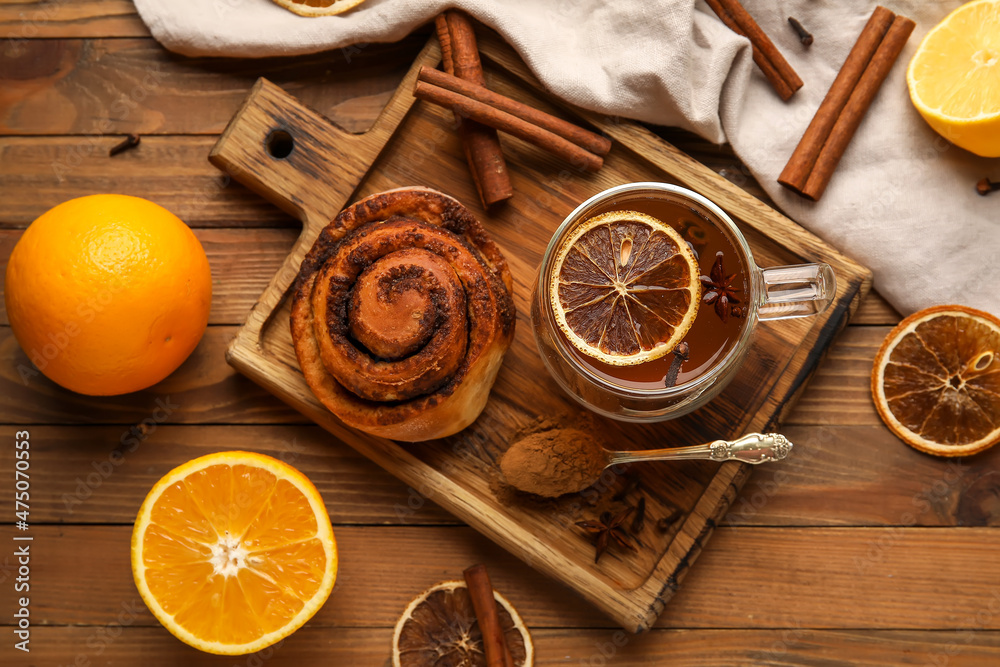 Wall mural glass cup of tasty orange tea with cinnamon and roll on wooden background