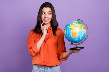 Portrait of attractive minded cheerful girl holding exploring globe thinking isolated over bright purple violet color background