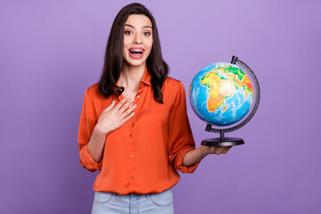 Portrait of attractive impressed cheerful girl holding studying globe isolated over bright purple...
