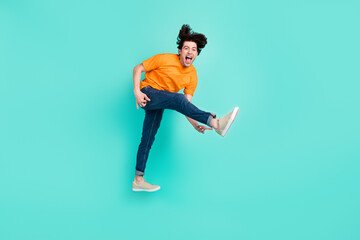Full length photo of cool brown hair millennial guy jump yell wear t-shirt jeans sneakers isolated on blue background