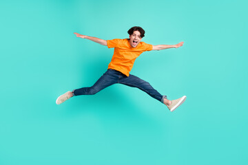 Fototapeta na wymiar Full body photo of crazy brown hair millennial guy jump yell wear t-shirt jeans sneakers isolated on blue background