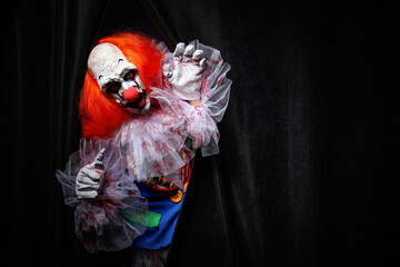 Terrifying clown hiding behind black curtains, space for text. Halloween party costume