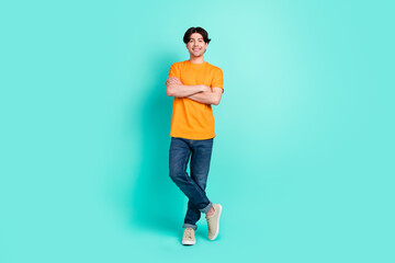 Fototapeta na wymiar Full size photo of cool brown hair young guy crossed arms wear t-shirt jeans sneakers isolated on blue background