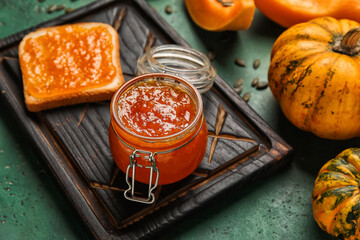 Jar of sweet pumpkin jam on green background