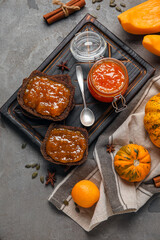 Jar of sweet pumpkin jam with orange and toasts on grey background