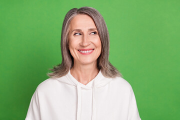 Photo of pretty thoughtful old woman dressed white sweatshirt smiling looking empty space isolated green color background