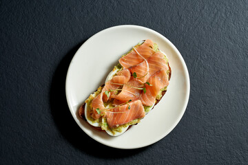 Toast with salmon and avocado mousse in a white plate on a black background