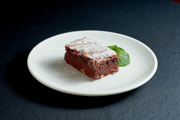 Brownie cake with nuts in a white plate on a dark background.