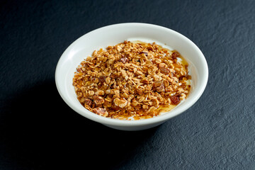 Healthy breakfast - granola with honey and yogurt in a white plate on a black background