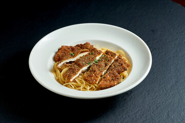 Breaded austrian schnitzel with pasta garnish in a white plate on a black background