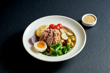 Diet nicoise salad with tuna, egg and asparagus in a white plate on a black background