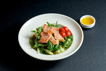 Diet salad with tomatoes and salmon in a white plate on a black background
