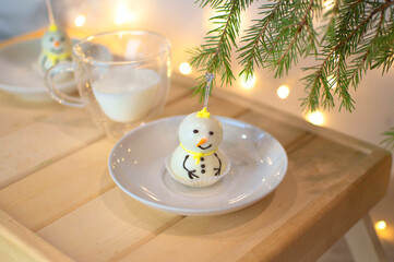 Snowman cupcake. Snowman almond cookies. Spruce branches against the background of garlands. Merry Christmas. Christmas mood. Sweet New Year's pastries. Selective focus.