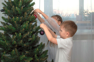 Brother and sister decorate the Christmas tree together. Celebrating a Christmas party. The child decorates the Christmas tree at home. A family with children celebrates the winter holidays