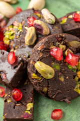 Aerial view of pieces of pistachio and pomegranate chocolate nougat, on green plate, selective focus, vertical