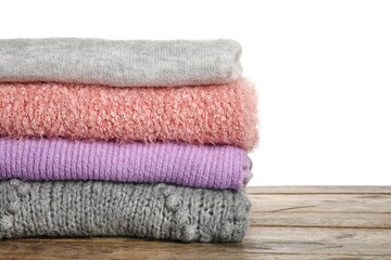 Fototapeta na wymiar Stack of warm soft sweaters on wooden table against white background, closeup