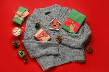 Stylish sweater, cup of cacao with marshmallows, gift boxes and Christmas decor on red background