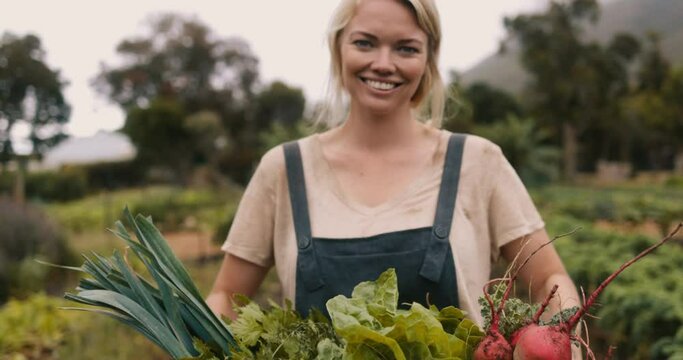 Self-sustainable female farmer holding a box full of fresh vegetable produce on her farm. Happy young farmer smiling at the camera after a successful harvest in her vegetable garden.