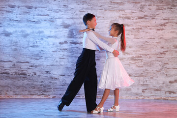 Beautifully dressed couple of kids dancing together in studio - obrazy, fototapety, plakaty