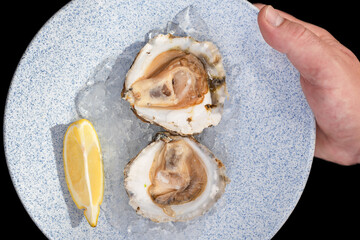 Plate of oysters with ice and lemon held by a hand on a black background