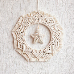 Christmas decor. Macrame wreath for Christmas and the new year on a white decorative plaster wall. Natural cotton thread, linen tape. Eco decor for home. Copy space