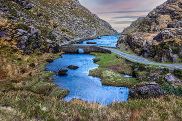 Fototapeta na wymiar Stone Wishing Bridge over winding stream in green valley at Gap of Dunloe in Black Valley of Ring of Kerry, County Kerry, Ireland