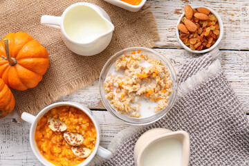 Pot and bowl of tasty oatmeal with pumpkin on white wooden background
