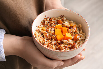 Woman holding bowl of tasty oatmeal with pumpkin, closeup