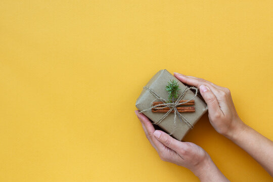Zero waste Christmas concept. Natural gift materials paper fir branches dried citrus cinnamon on a yellow background. A gift in women's hands. Eco-greeting card in pastel colors. Gifts New Year 2022