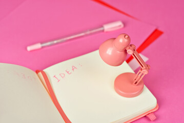 Notebook on a pink background. Toy table lamp near the notebook. Copy space and free space for text in notebook. Mockup for design. The word 