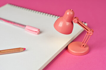 Notepad on a pink background. Toy table lamp near the notebook. Copy space and free space for text near the lamp. The concept of roochy space and creative ideas.
