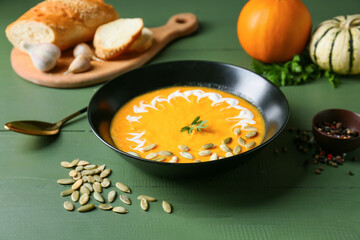 Bowl with delicious pumpkin cream soup and seeds on color wooden background