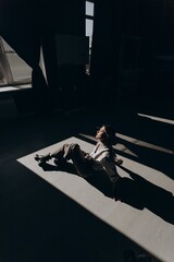 Portrait of fashion retro girl in white shirt, suspenders and brown wide pants sitting on floor in the sun in room