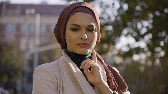 A young beautiful Muslim woman thinks about something and nods in a park in an urban area - closeup
