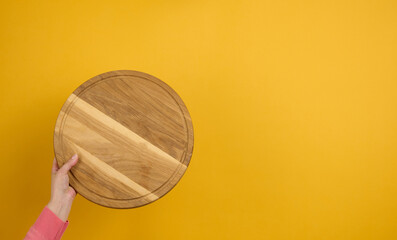 woman holding empty round wooden pizza board in hand, body part  on a yellow background