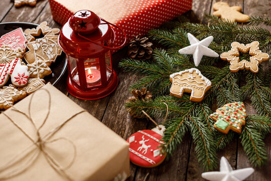 Winter holiday gifts and homemade tasty cookies with sugar icing on wooden table along with red festive lantern and other winter motives, merry Christmas