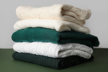Fototapeta na wymiar Stack of stylish knitted sweaters on green table against grey background