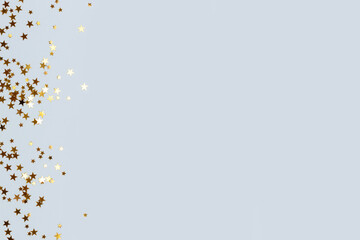 Bright gold glittering stars confetti scattered on a blue pastel background with place for text.