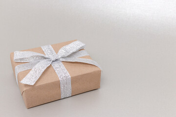 Gift box in front of silver colored background. Present with tied ribbon.