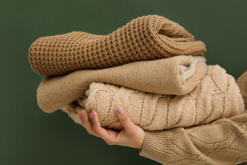 Woman holding stack of stylish sweaters on green background