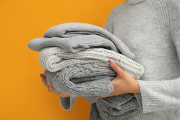 Woman holding stack of stylish sweaters on color background