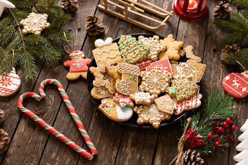 Plate full of traditionally shaped Christmas cookies glazed in sugar icing winter holiday themes placed on a wooden table decorated in concept of Christmas