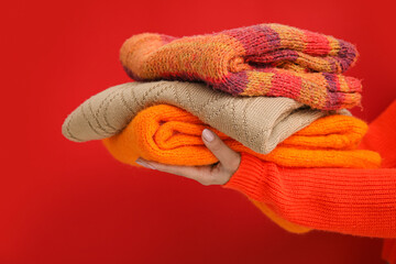Young woman holding different knitted sweaters on color background
